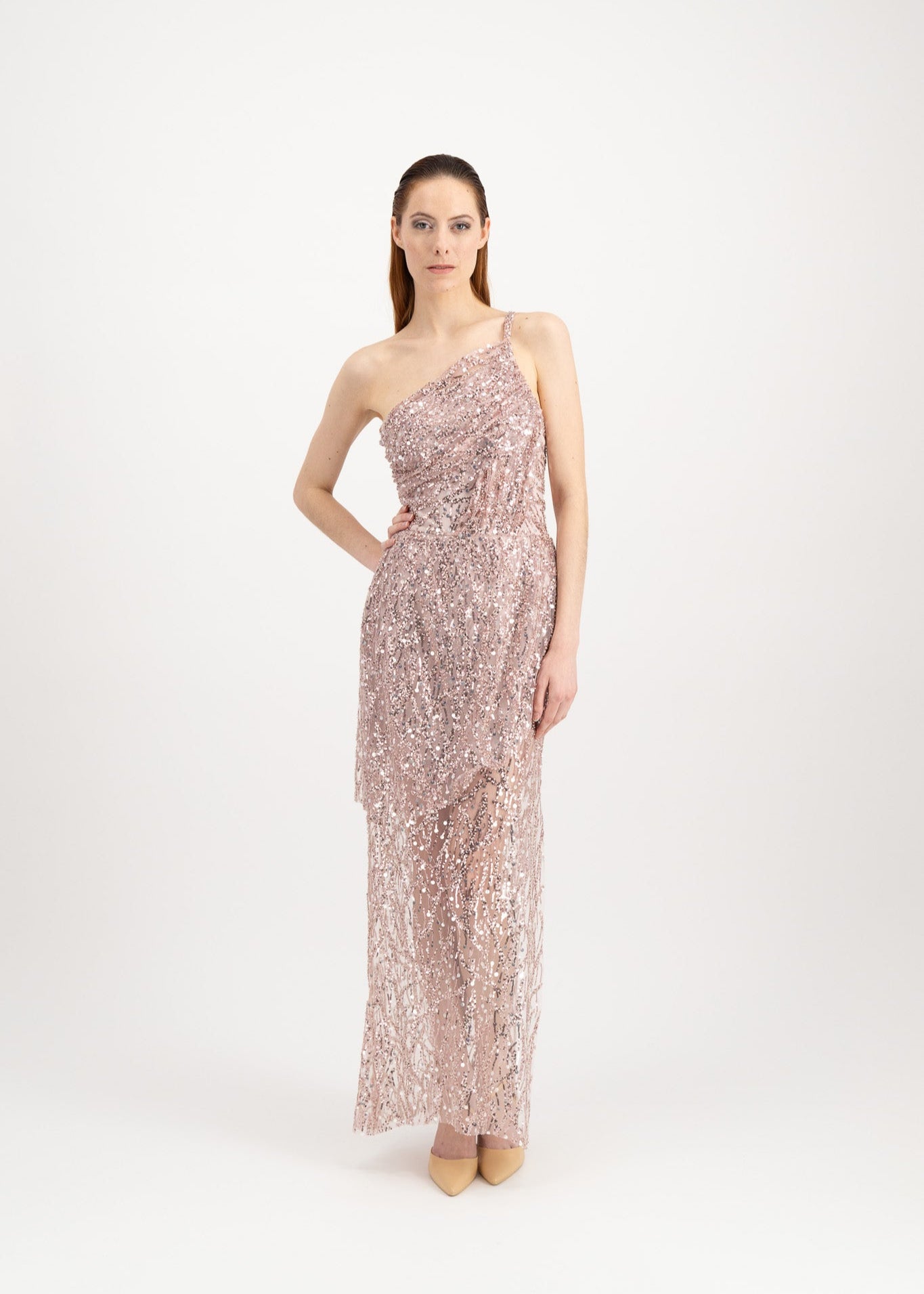 Jeune femme rousse habillée d'une longue robe du soir rose et brillante avec une fente et portée par une seule bretelle