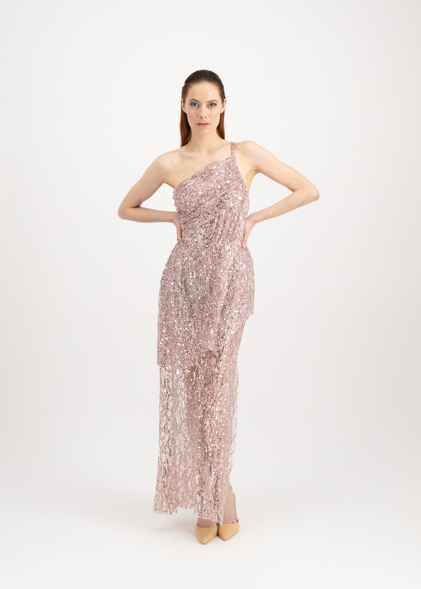 Jeune femme rousse habillée d'une longue robe du soir rose et brillante avec une fente et portée par une seule bretelle