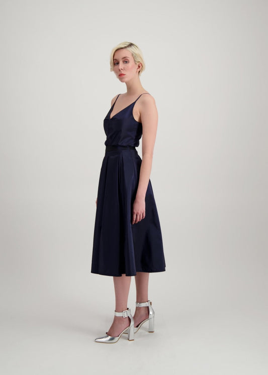 Femme blonde de profil habillée d'un ensemble bleu avec un top à bretelles et d'une jupe midi