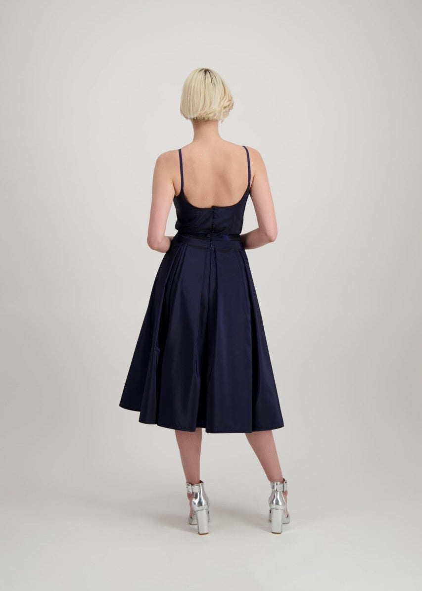 Femme blonde de dos habillée d'un ensemble bleu marine avec un top à bretelles et d'une jupe
