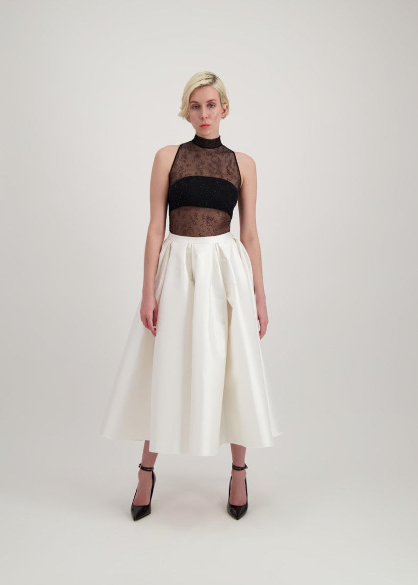 Femme blonde habillée d'une jupe midi blanche et d'un body transparent noir laissant apparaître un bandeau noir