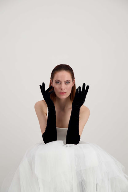 Jeune femme rousse, les mains aux oreilles, habillée d'une robe blanche et d'une paire de gants en velours noir
