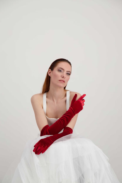 Jeune femme rousse qui se tient l'épaule. Elle porte des longs gants en velours rouges
