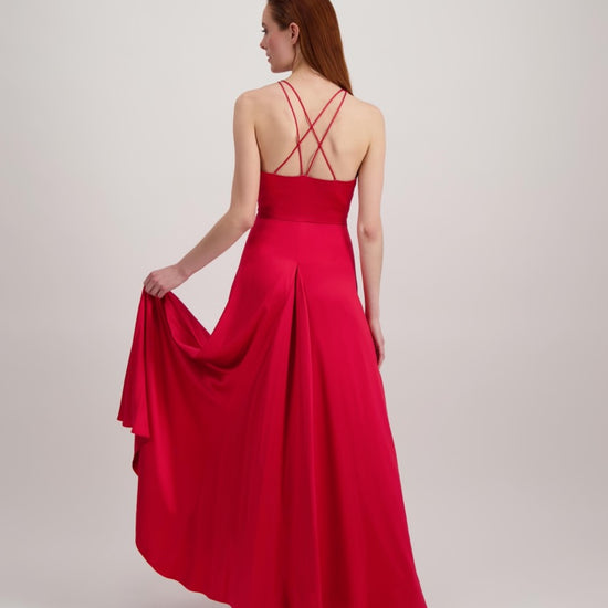 Jeune femme rousse qui marche avec une longue robe rouge très évasée en bas et un dos ouvert où se croisent de fines bretelles