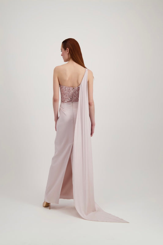 Jeune femme rousse de dos qui porte une longue robe rose avec une étole qui finit en traîne