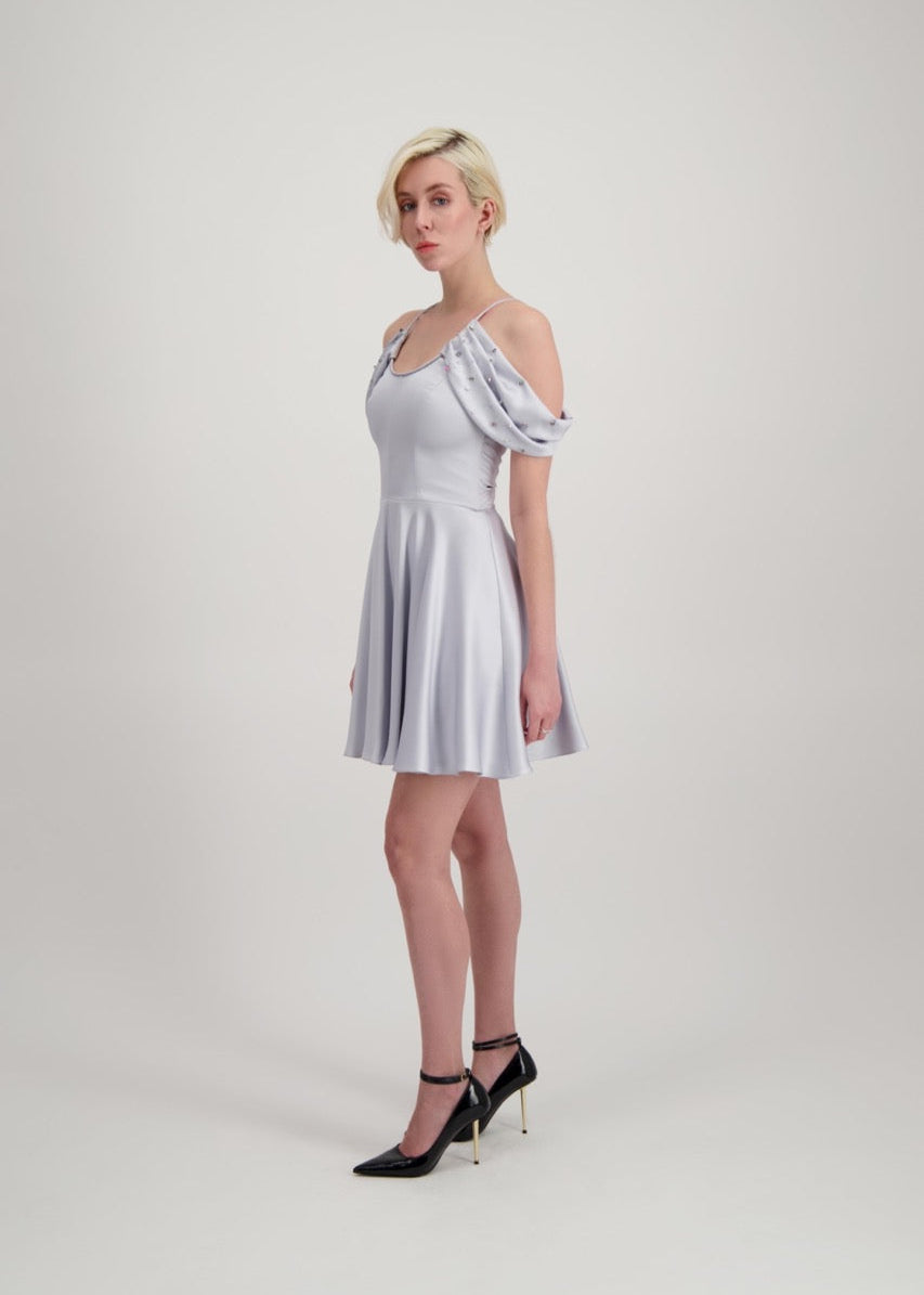 Jeune femme blonde de profil habillée d'une robe coktail courte de couleur argent avec des strass sur les épaules