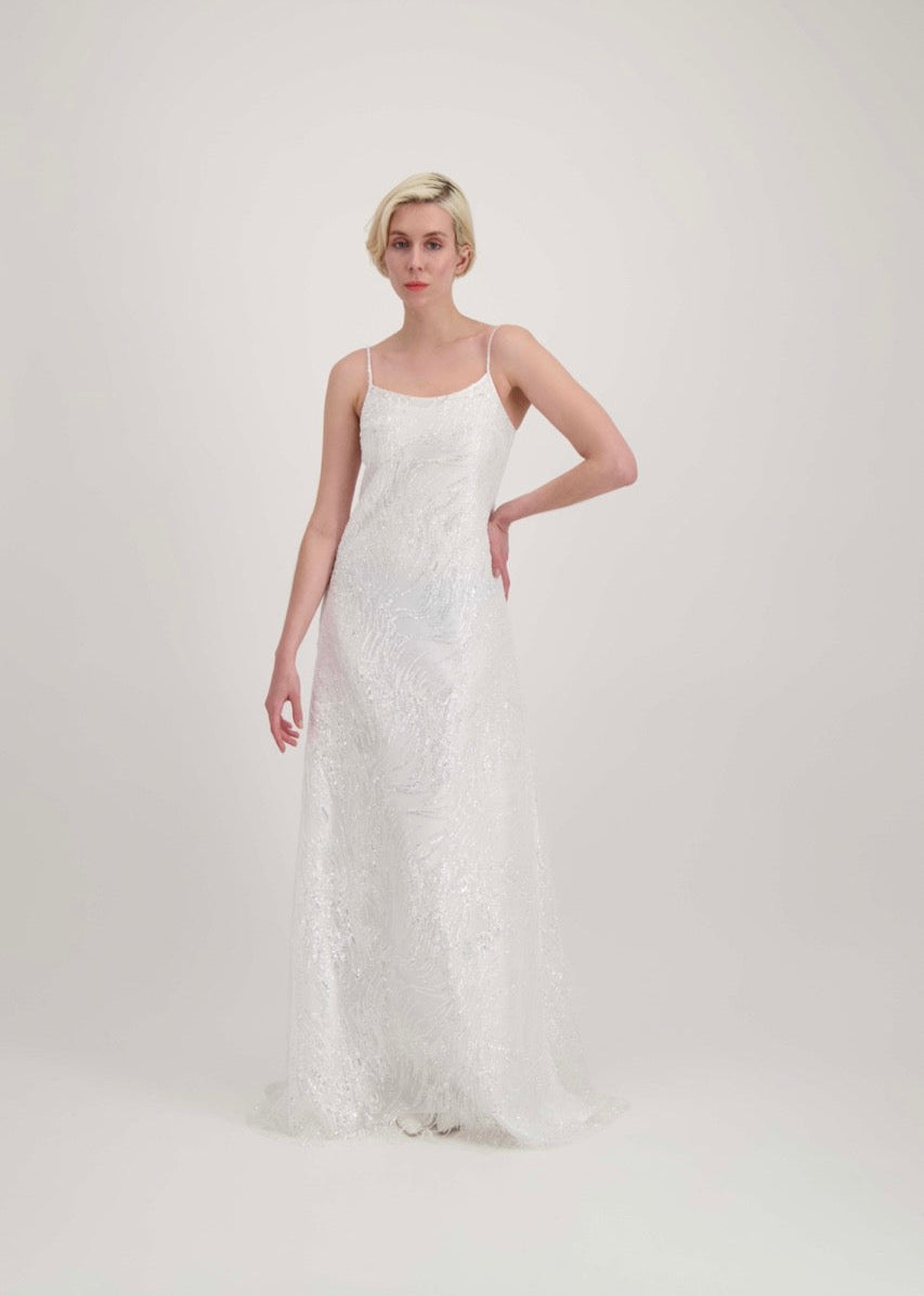 Jeune femme blonde avec une main à la taille habillée d'une robe de mariée blanche à fines bretelles