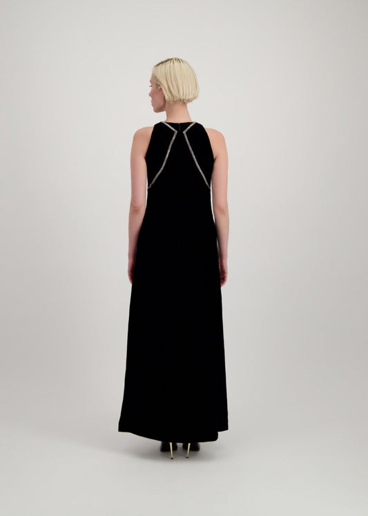 Jeune femme blonde de dos habillée d'une robe longue en velours noir avec des chevrons de strass et une fente