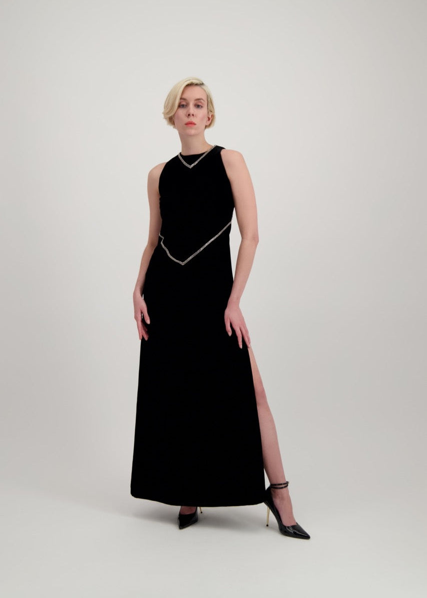 Jeune femme blonde habillée d'une robe longue en velours noir avec des chevrons de strass et une fente