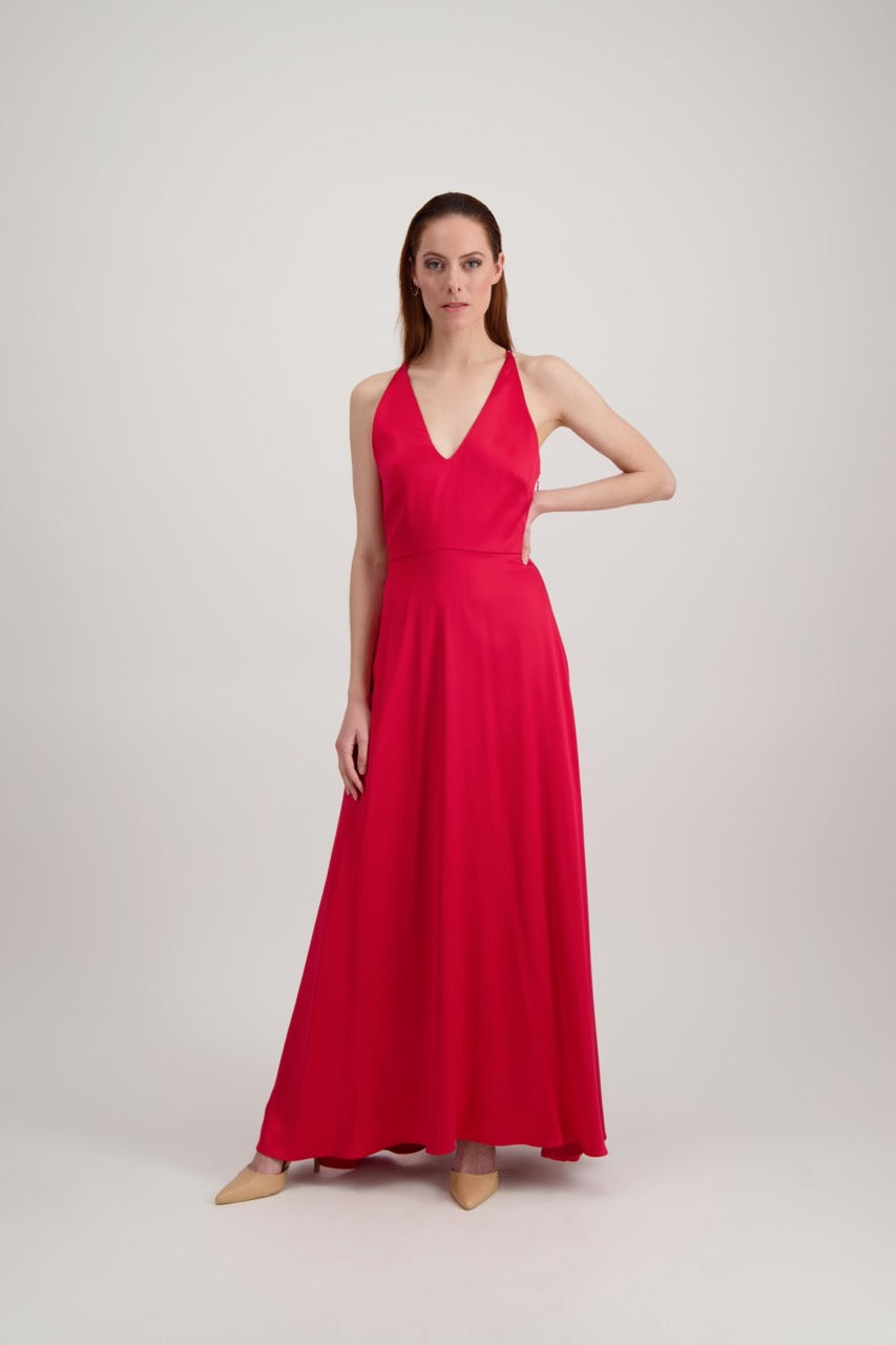 Jeune femme rousse habillée d'une longue robe rouge avec un col en V. Elle se tient avec un coude à la taille