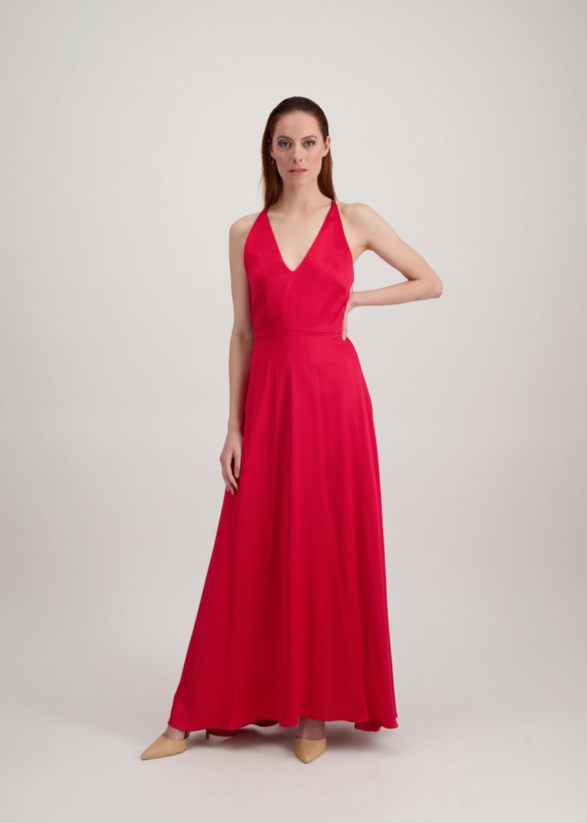 Jeune femme rousse habillée d'une longue robe rouge avec un col en V. Elle se tient avec un coude à la taille