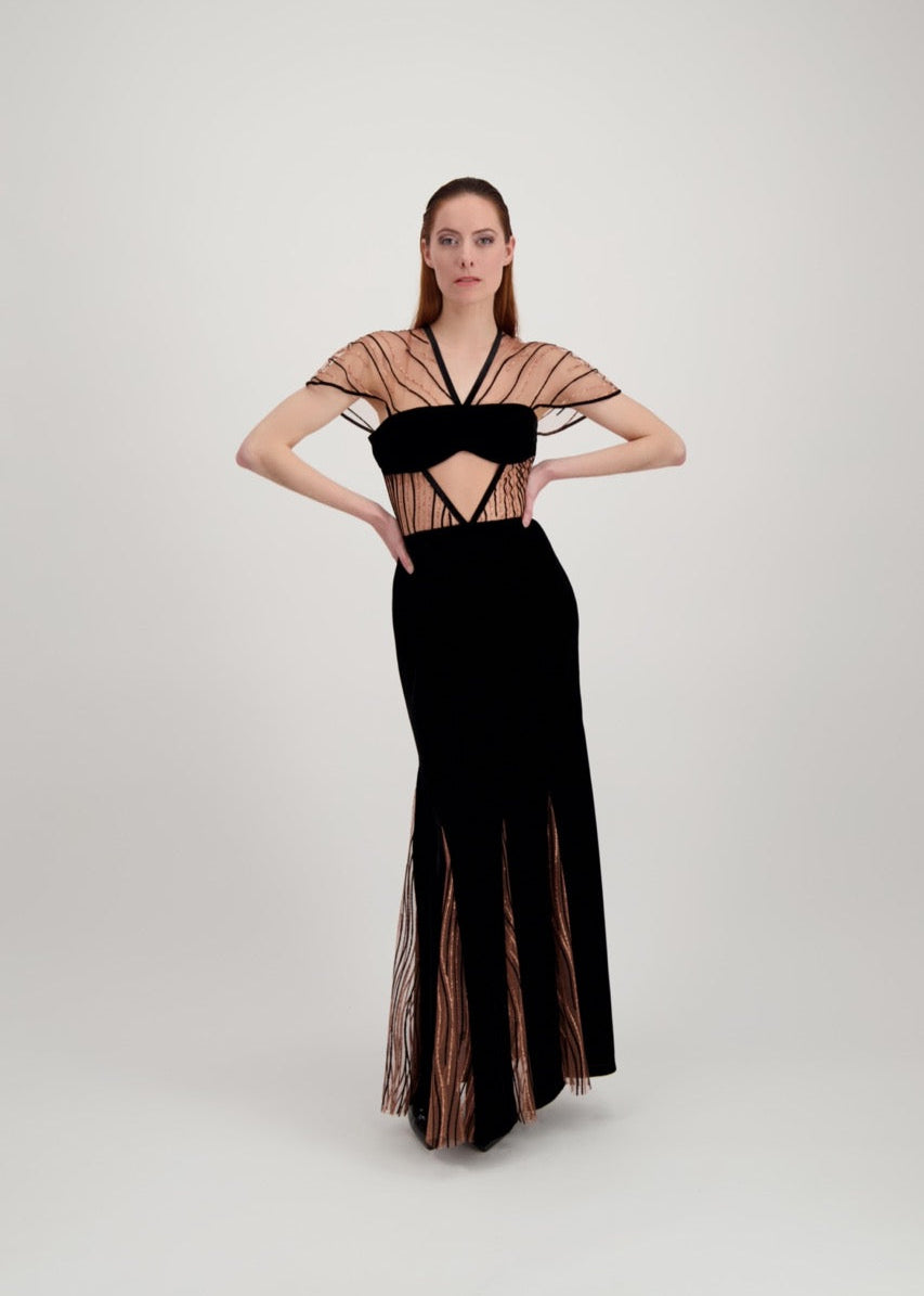 Jeune femme rousse habillée d'une longue robe du soir en velours noir avec des motifs ondulés brillants.