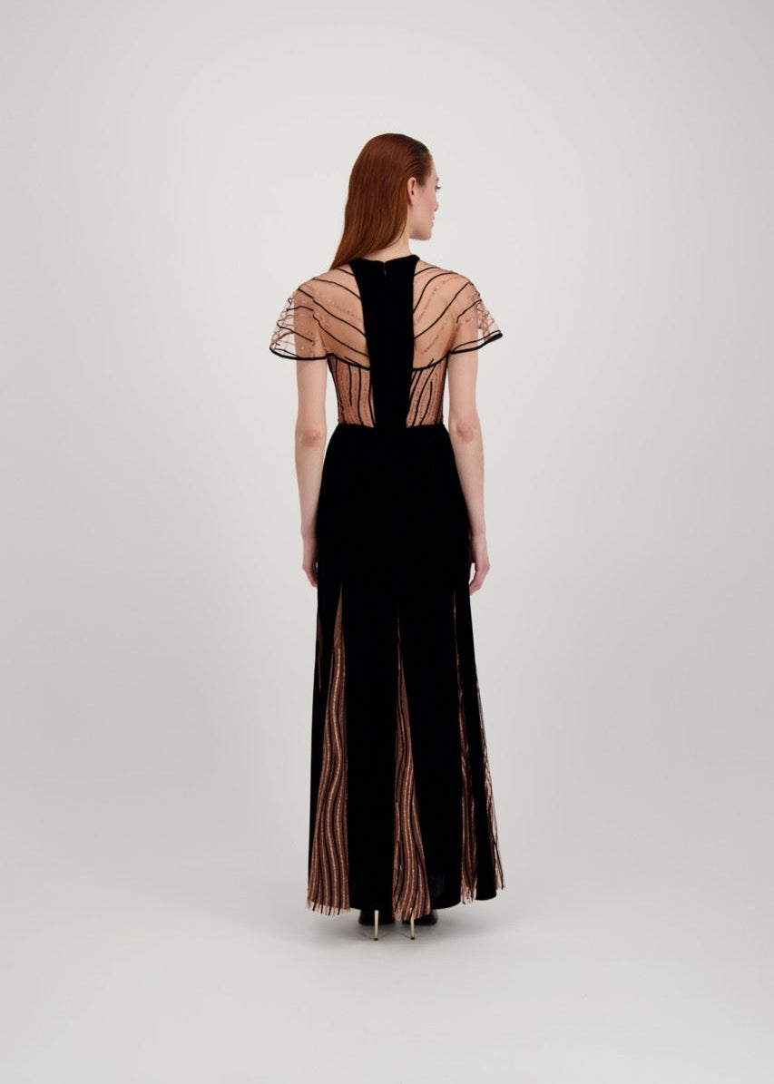 Jeune femme rousse de dos habillée d'une longue robe du soir en velours noir avec des motifs ondulés brillants.