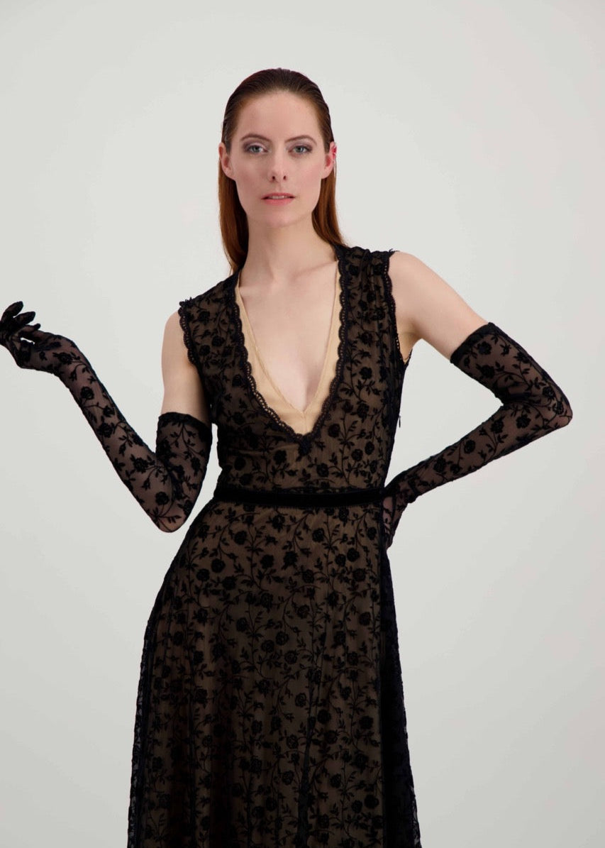 Jeune femme rousse habillée d'une robe en dentelle noire et d'une paire de longs gants assortis.