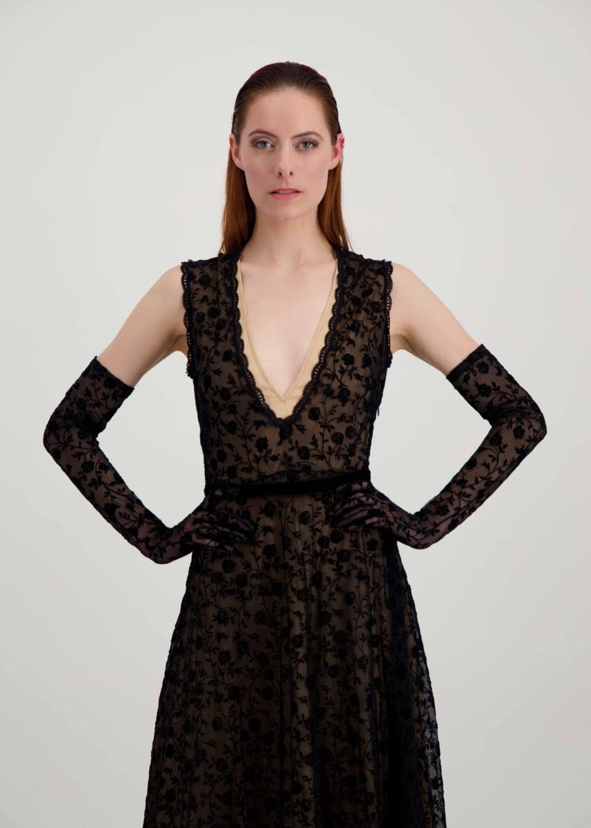Jeune femme rousse qui a les mains sur les hanches. Elle est habillée avec une robe en dentelle noire et des longs gants assortis