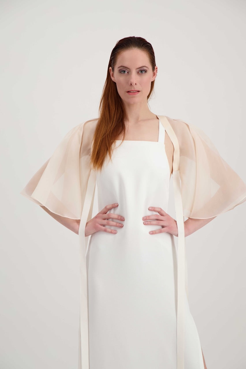 Jeune femme rousse habillée d'une robe blanche et d'une cape rose poudré avec des lanières en soie.