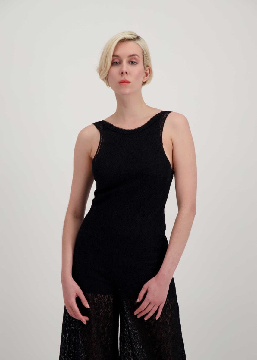 Femme blonde portant une combinaison pantalon en dentelle noire, sans manche et légèrement transparente