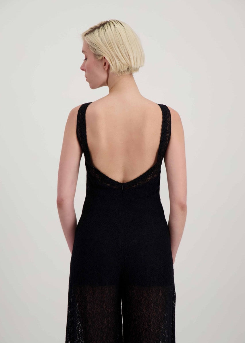 Femme blonde de dos portant une combinaison pantalon en dentelle noire avec un dos nu.