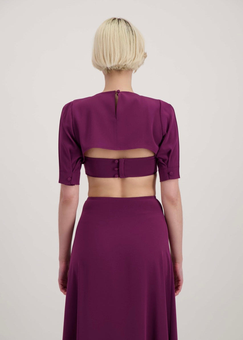 Femme blonde de dos habillée avec un ensemble composé d'un boléro, d'un bandeau et d'une jupe lila