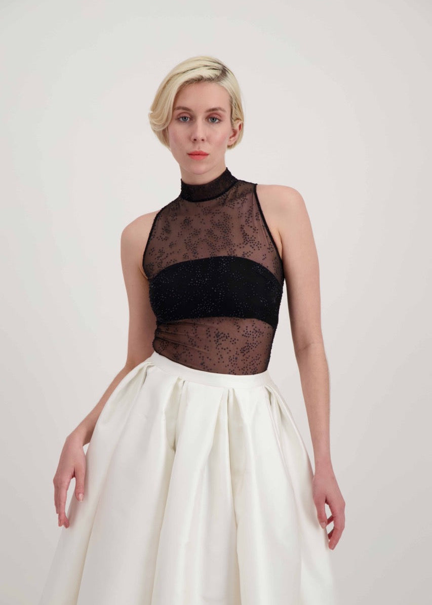 Femme blonde habillée d'une jupe blanche et d'un body transparent noir laissant apparaître un bandeau noir