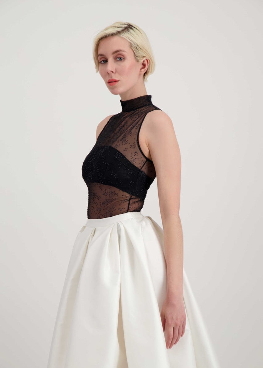 Femme blonde de profil habillée d'une jupe blanche et d'un body transparent noir laissant apparaître un bandeau noir