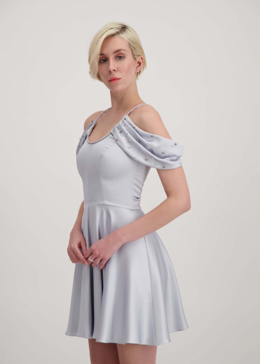 Jeune femme blonde de profil habillée d'une robe coktail courte de couleur argent avec des strass sur les épaules