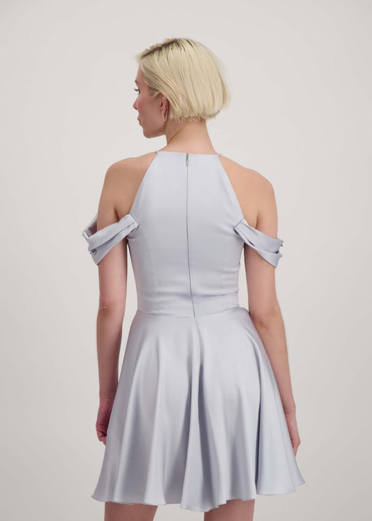 Jeune femme blonde de dos habillée d'une robe coktail courte de couleur argent avec des strass sur les épaules