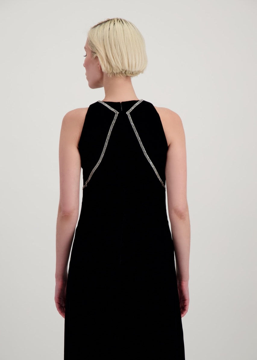 Jeune femme blonde de dos habillée d'une robe longue en velours noir avec des chevrons de strass et une fente