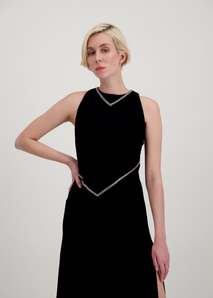 Jeune femme blonde, une main sur la taille, habillée d'une robe longue en velours noir avec des chevrons de strass et une fente