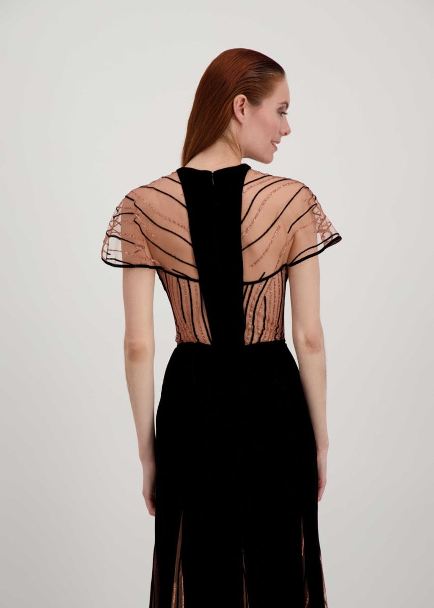 Jeune femme rousse de dos habillée d'une longue robe du soir en velours noir avec des motifs ondulés brillants.