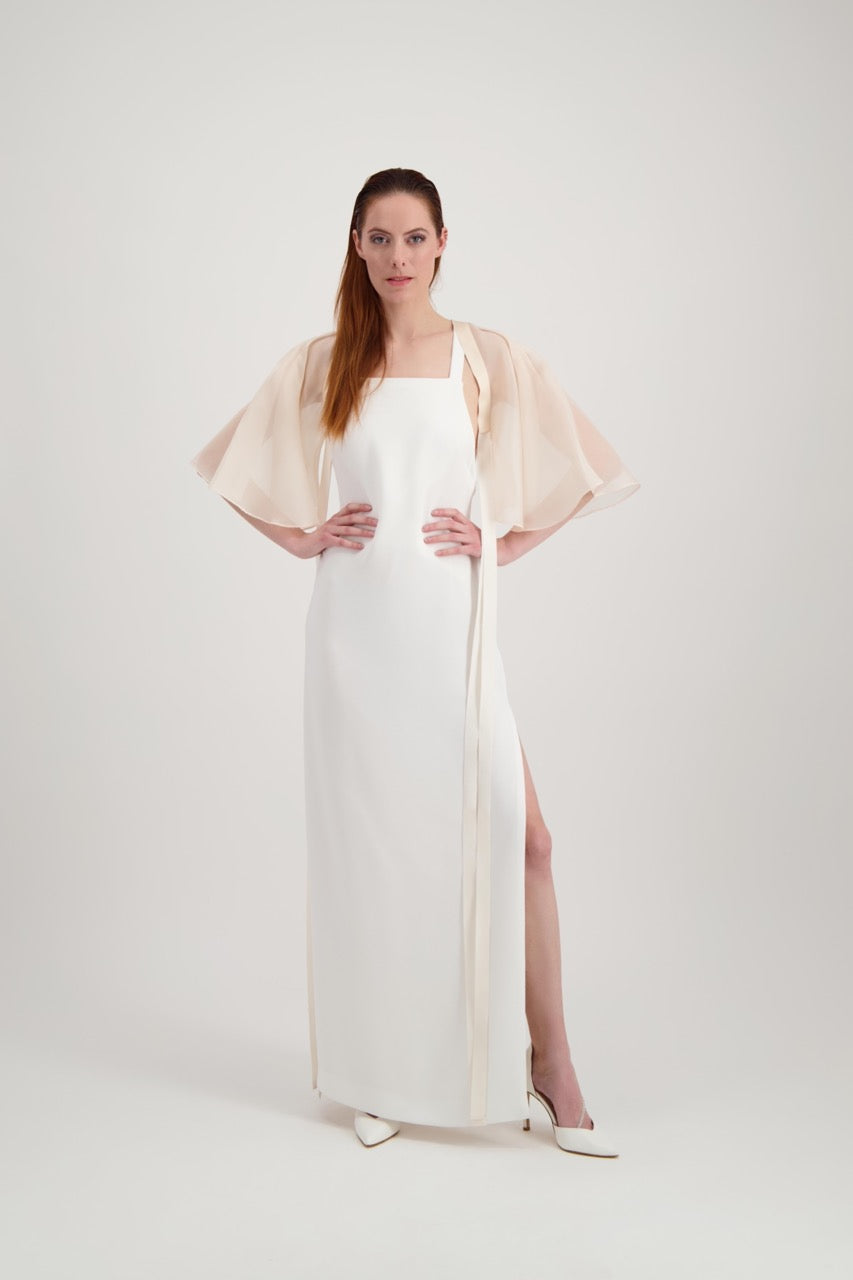 Jeune femme rousse habillée d'une robe blanche et d'une cape rose poudré avec des lanières en soie.