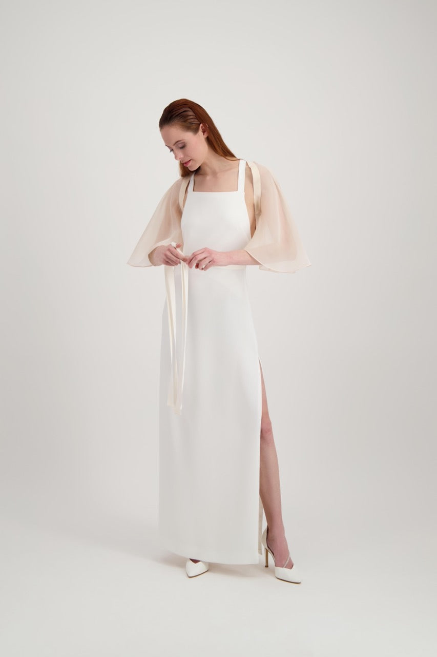 Jeune femme rousse habillée d'une longue robe blanche et nouant une cape rose poudrée à l'aide de rubans de soie