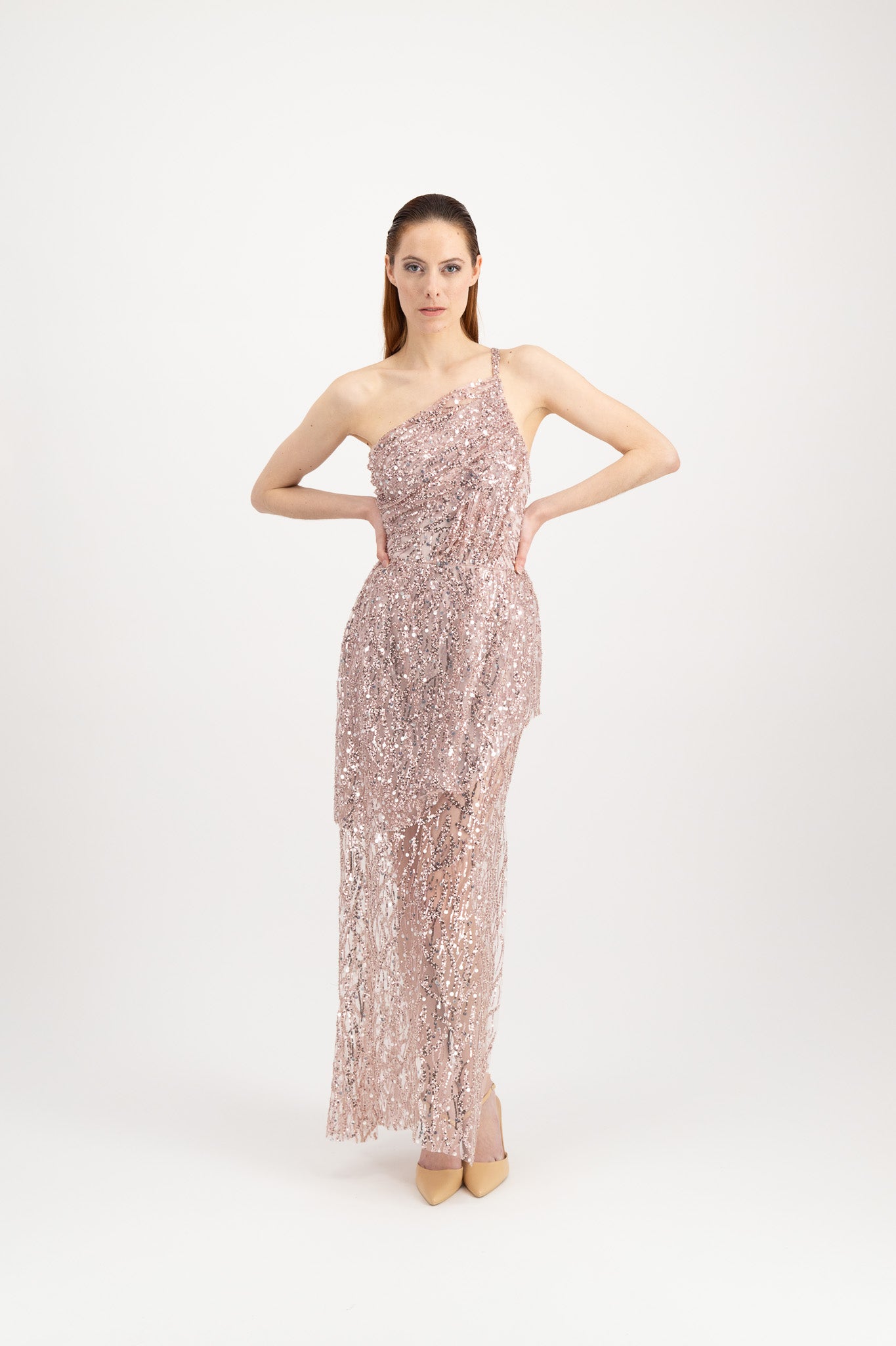 Jeune femme rousse habillée d'une longue robe du soir rose et brillante avec une fente et portée par une seule bretelle