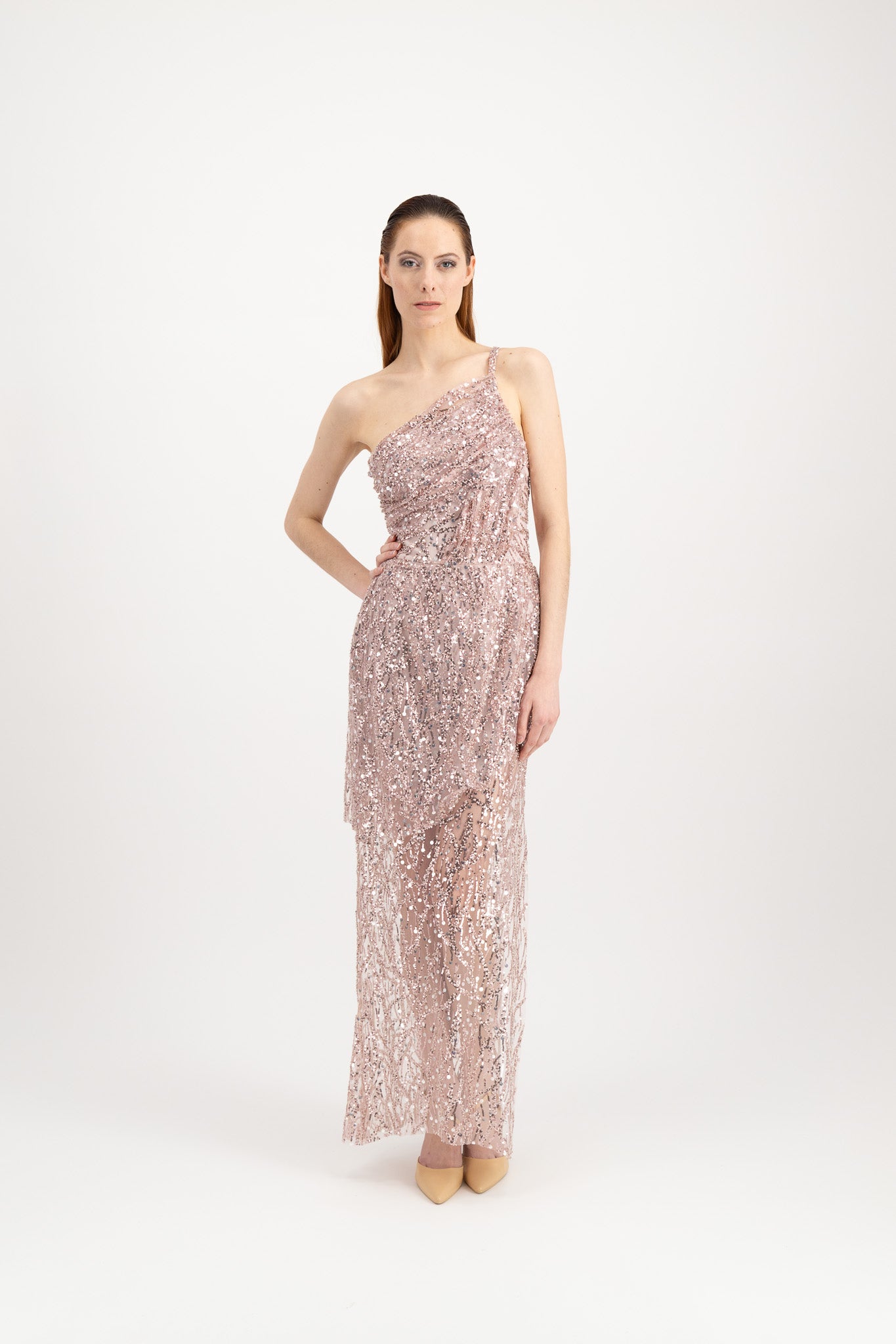 Jeune femme rousse habillée d'une longue robe du soir rose et brillante avec une fente et portée par une seule bretelle
