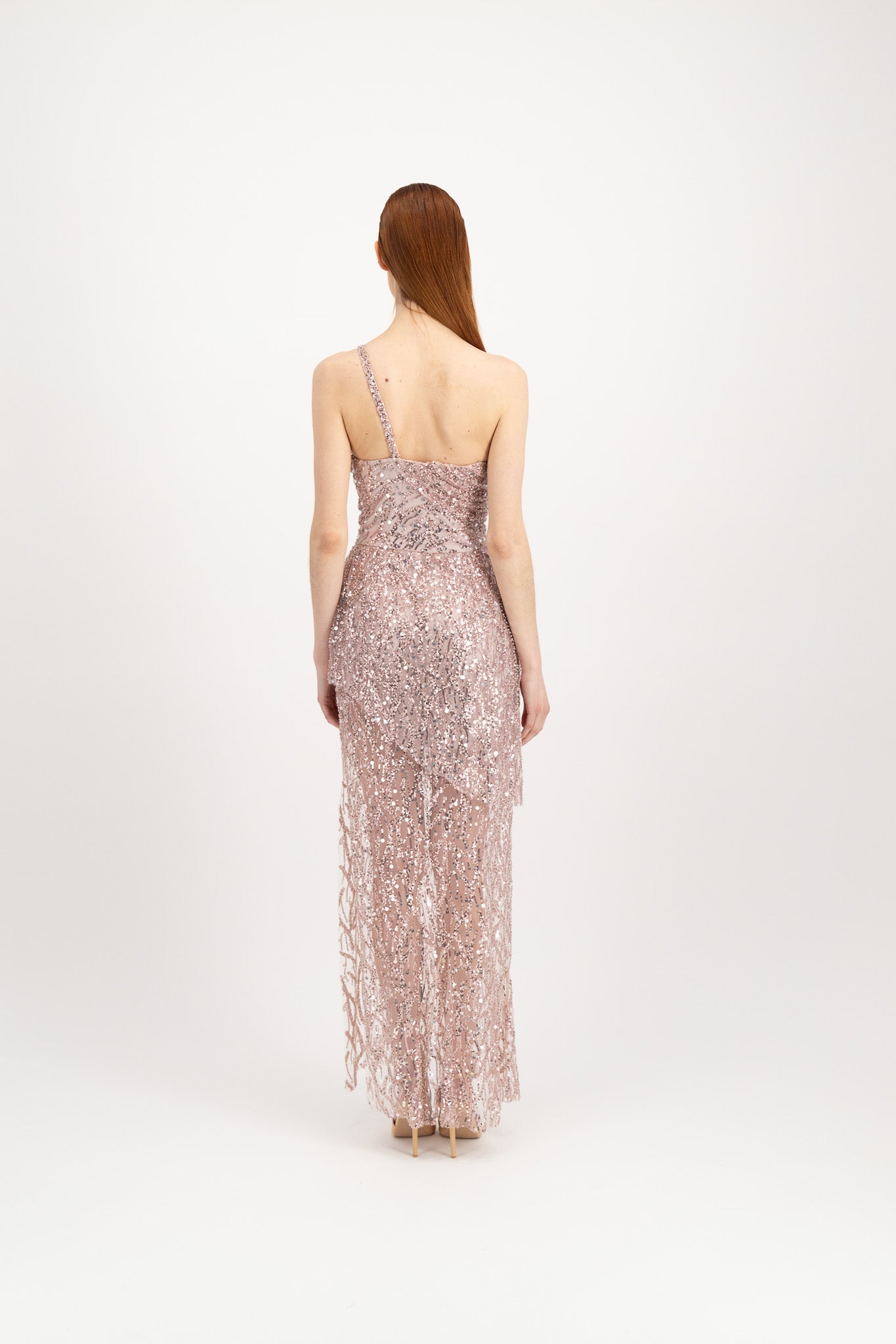 Jeune femme rousse habillée d'une longue robe du soir rose et brillante avec une fente et portée par une seule bretelle