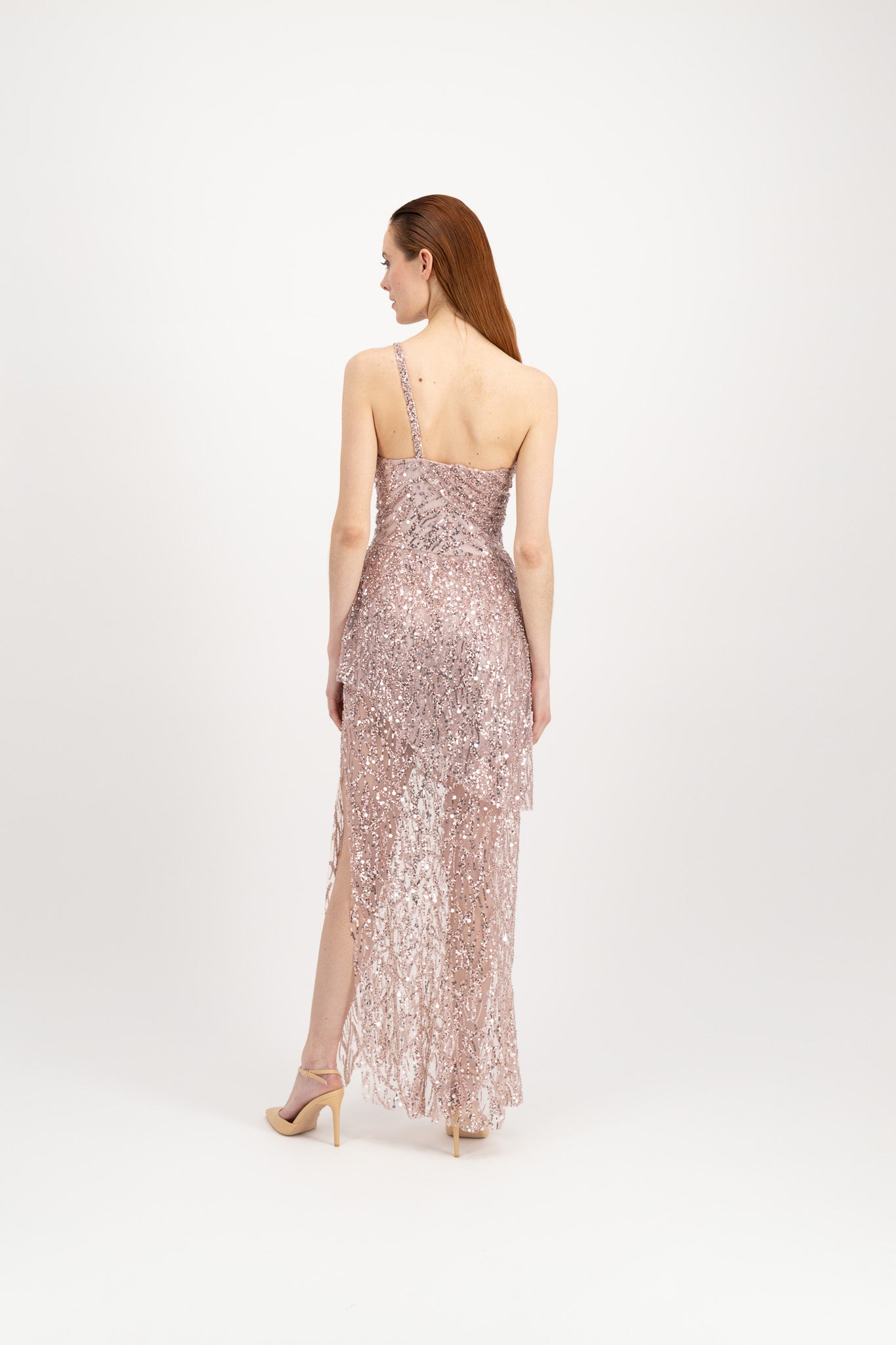 Jeune femme rousse habillée d'une longue robe du soir rose et brillante avec une fente et portée par une seule bretelle