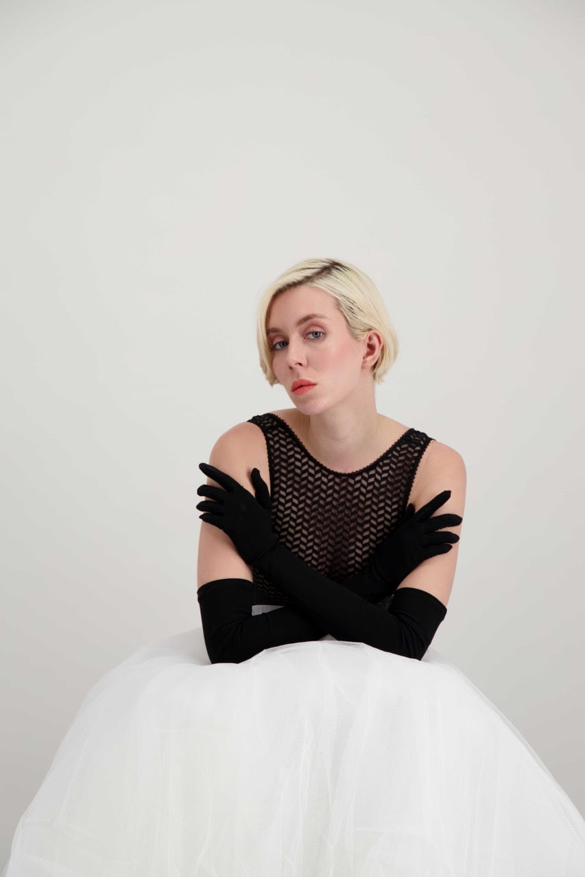 Jeune femme blonde portant de longs gants noirs qui pose les bras croisés