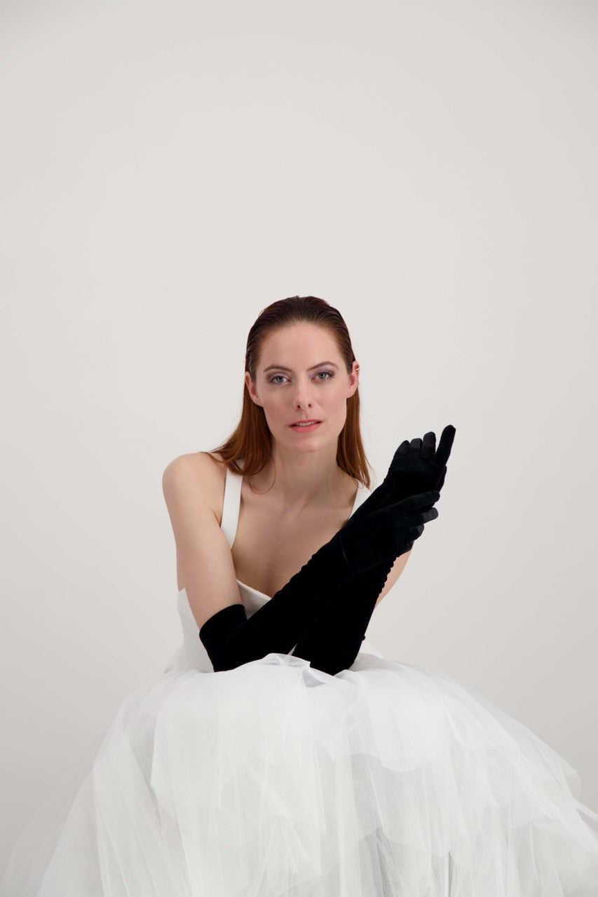 Jeune femme rousse qui s'attrape les mains. Elle porte des longs gants noirs en velours
