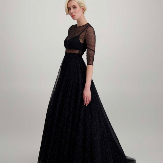 Jeune femme blonde habillée d'une longue robe noire brillante et d'un énorme jupon de tulle