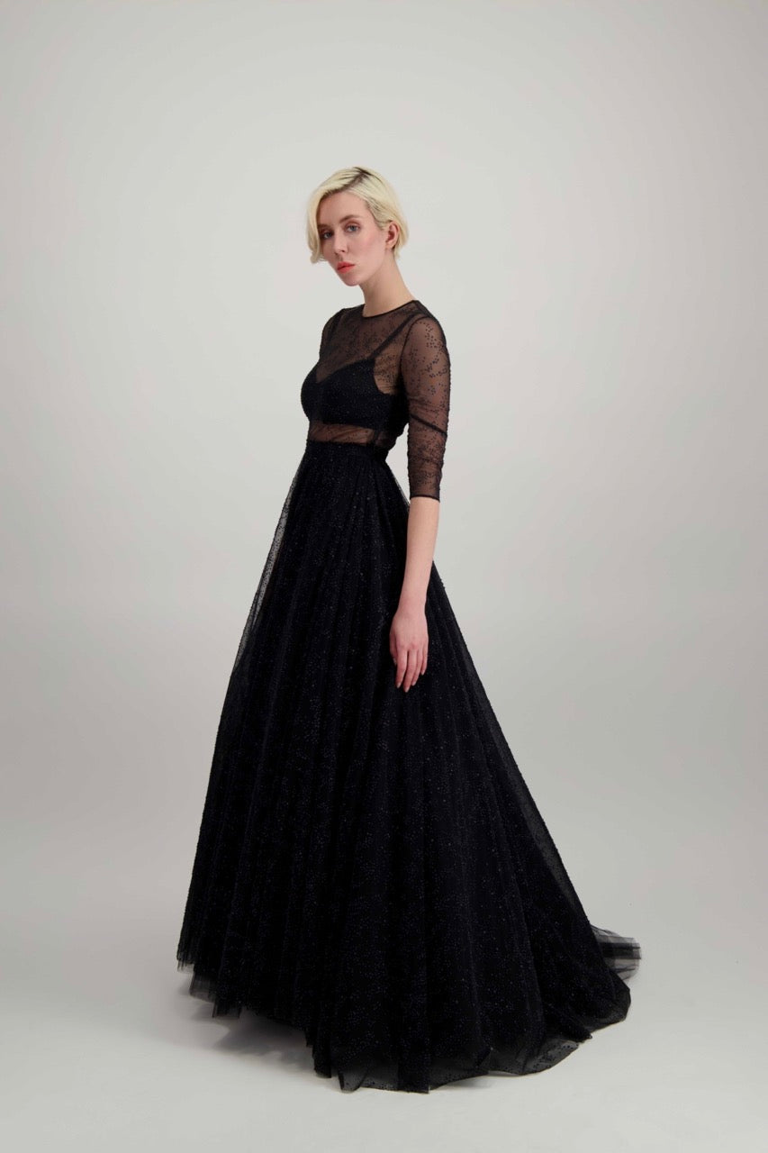 Jeune femme blonde habillée d'une longue robe noire brillante et d'un énorme jupon de tulle