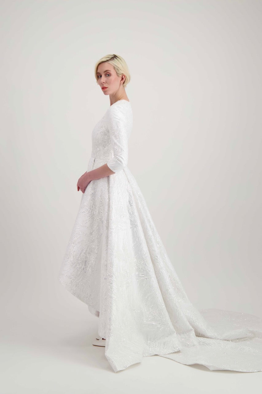 Jeune femme blonde marchant avec une robe de mariée blanche, courte devant et avec une longue traîne à l'arrière