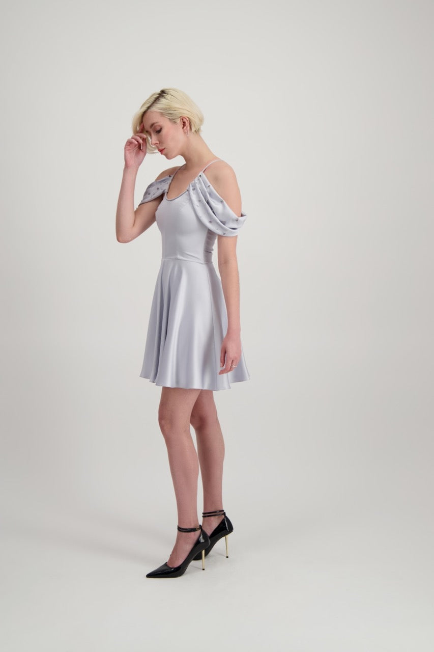 Jeune femme blonde qui tourne habillée d'une robe coktail courte de couleur argent avec des strass sur les épaules