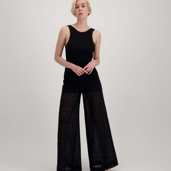 Femme blonde qui marche, habillée d'une combinaison pantalon ample noire avec un dos nu.