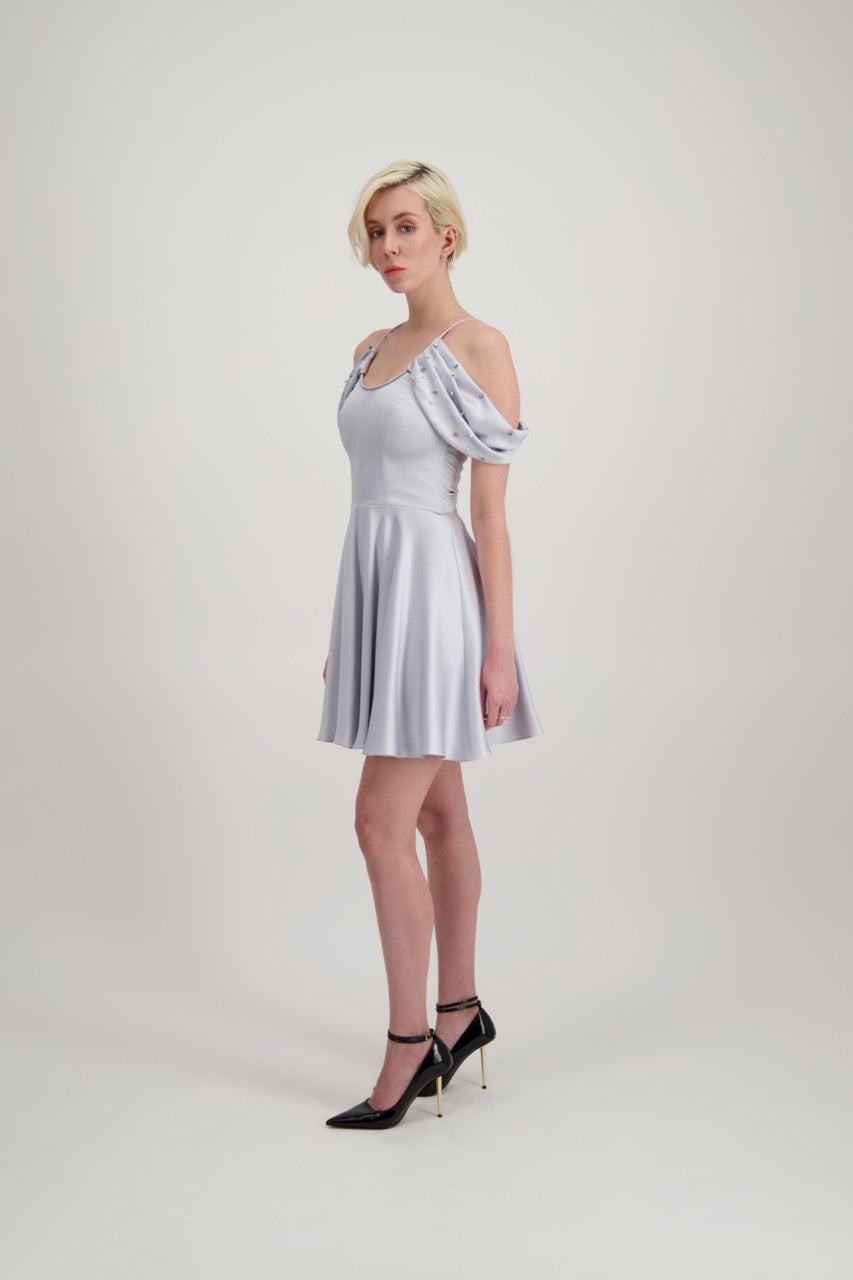 Jeune femme blonde de profil habillée d'une robe coktail courte de couleur argent avec des strass sur les épaules