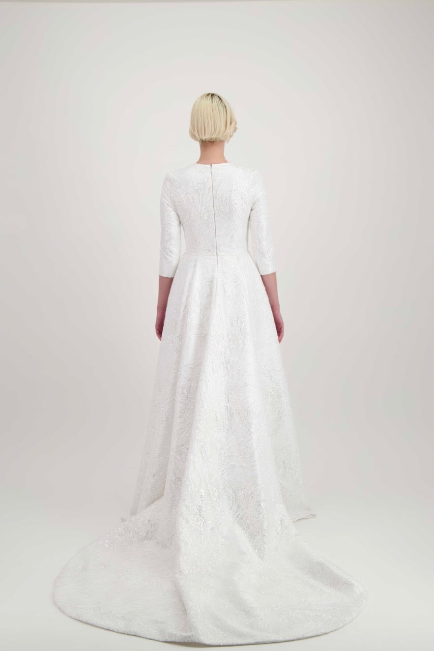 Jeune femme blonde habillée d'une robe de mariée avec une longue traîne et des manches 3/4
