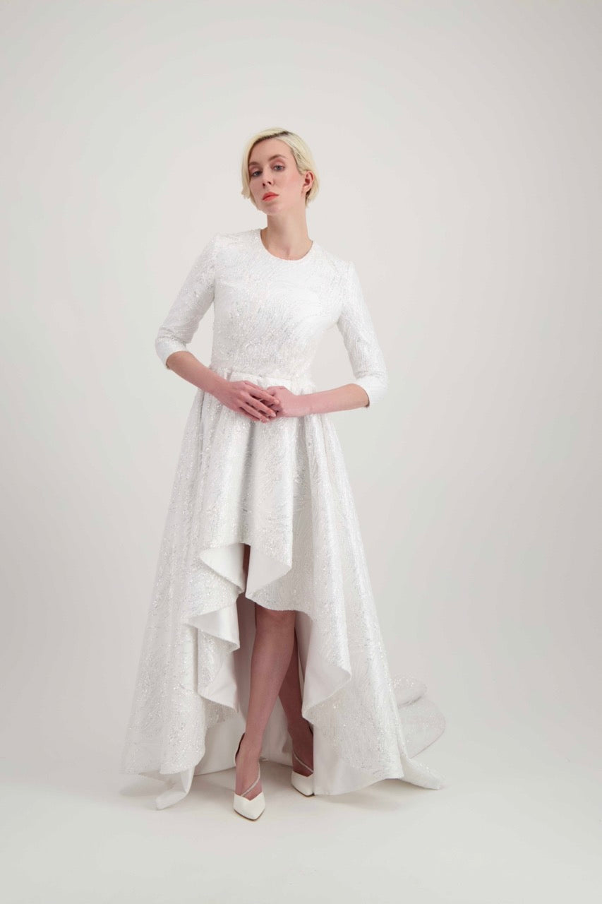 Jeune femme blonde habillée d'une robe de mariée blanche courte devant avec une longue traîne
