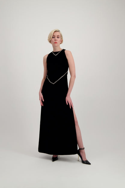Jeune femme blonde habillée d'une robe longue en velours noir avec des chevrons de strass et une fente 