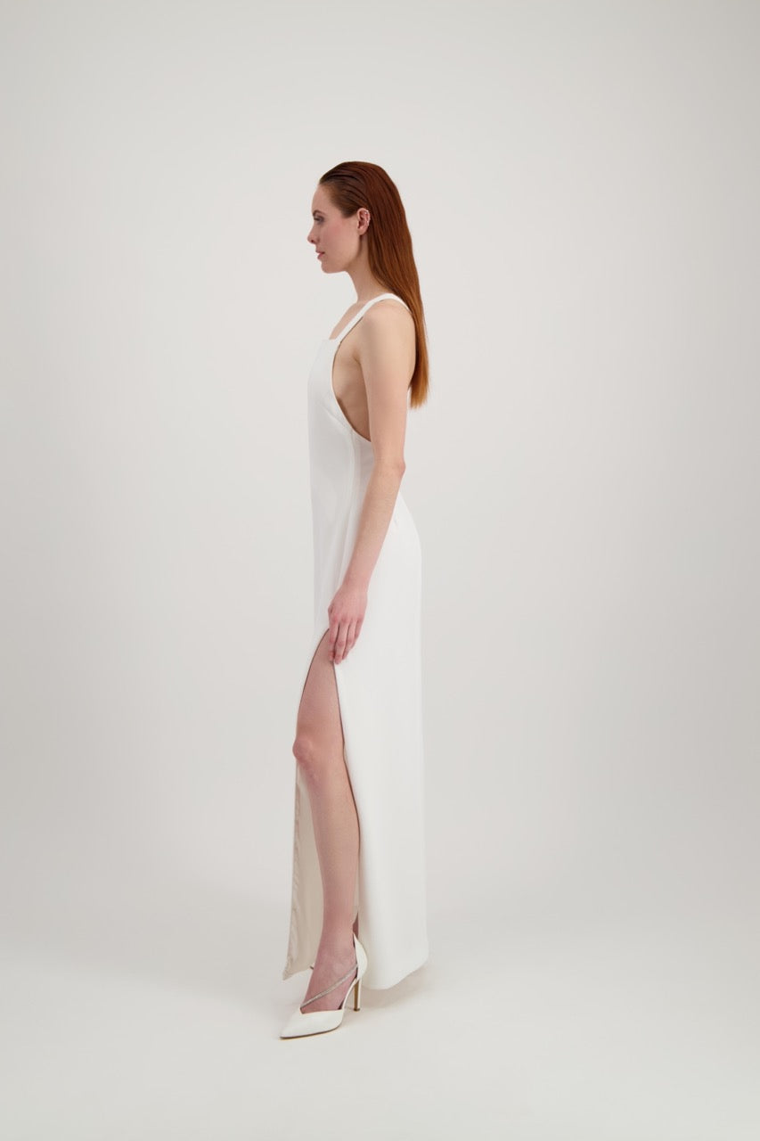 Jeune femme rousse habillée d'une longue robe blanche à larges bretelles avec une grande fente et un dos nu 