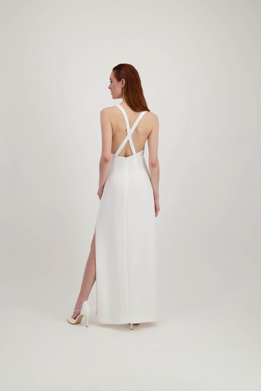 Jeune femme rousse de dos habillée d'une longue robe blanche avec une fente et un dos nu où se croisent des bretelles 