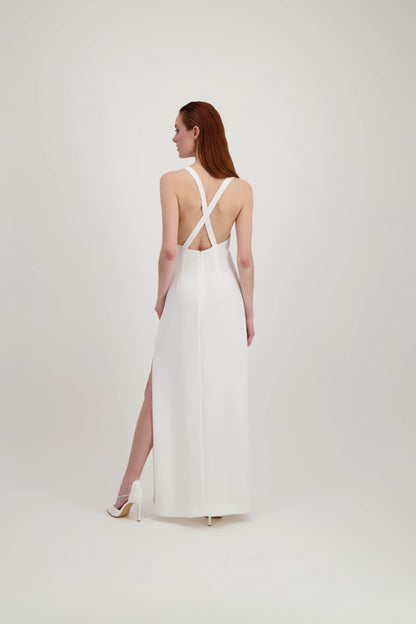 Jeune femme rousse de dos habillée d'une longue robe blanche avec une fente et un dos nu où se croisent des bretelles 